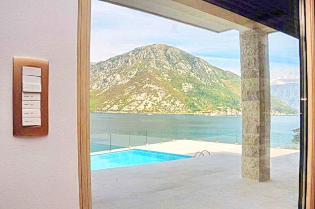 View from the living room of the pool and Kotor Bay in the Morinj residential complex, Montenegro: panoramic window, stone column, and terrace.