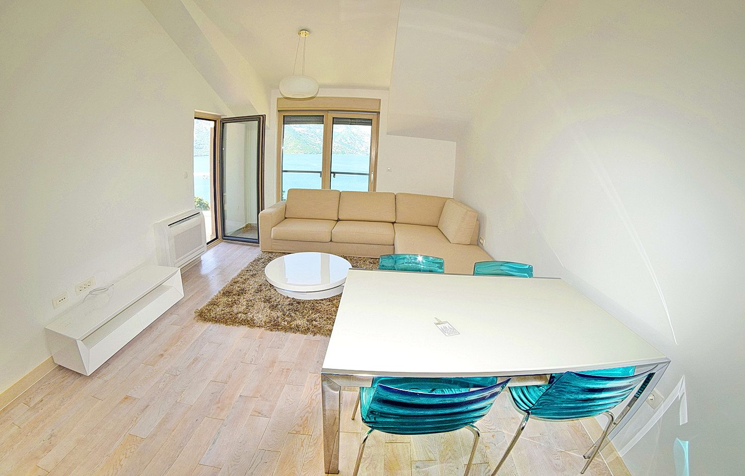 Bright living room in the Morinj residential complex, Montenegro: beige sofa, dining area with blue chairs, and sea view from the window.