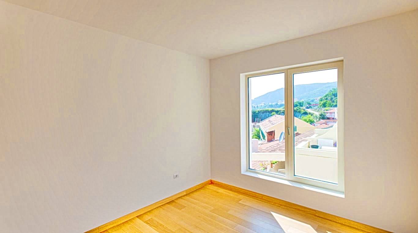 Bright empty bedroom with parquet flooring and a view of the mountains and the town of Rafailovici, Montenegro.
