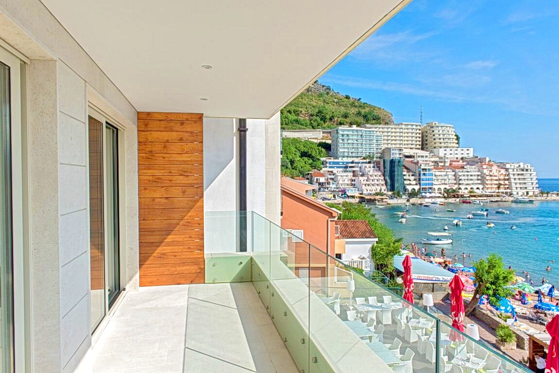 Spacious balcony with panoramic views of the sea and beach in Rafailovići, Montenegro, modern finishes and glass railings.