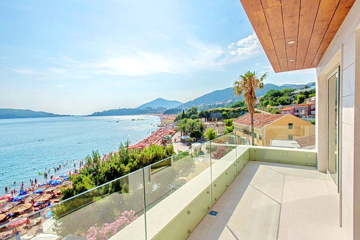Spacious balcony with panoramic views of the sea and beach in Rafailovići, Montenegro, modern finishes and glass railings.