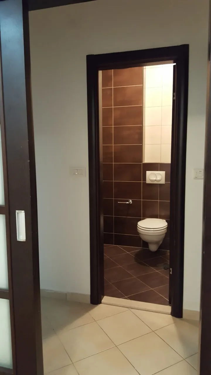 View through a doorway showing a wall-mounted toilet and walls tiled in brown and beige.