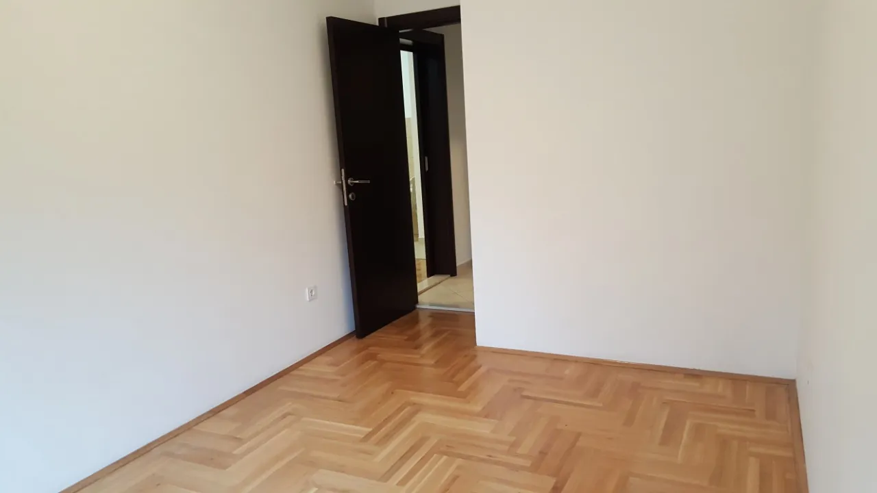 Empty room with herringbone parquet flooring and an open dark door, no furniture or specific room features visible.