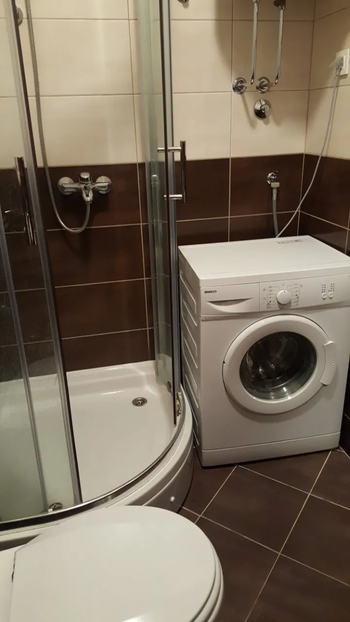 Bathroom featuring a corner shower enclosure, white washing machine, and toilet against tiled walls.