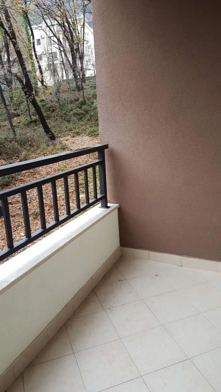 Empty balcony with tiled floor, black metal railing, and a view of trees and a neighboring building.
