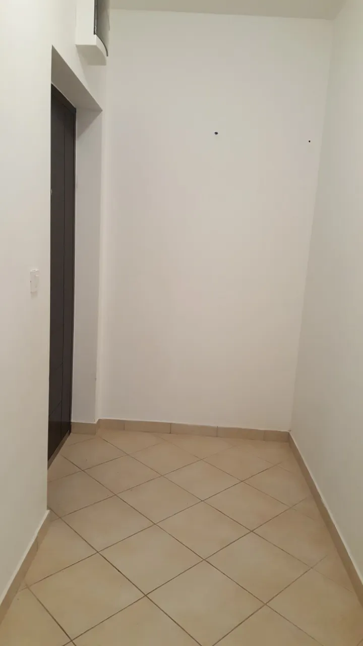 Empty hallway or entryway with beige floor tiles and white walls. A dark door frame is visible on the left side.