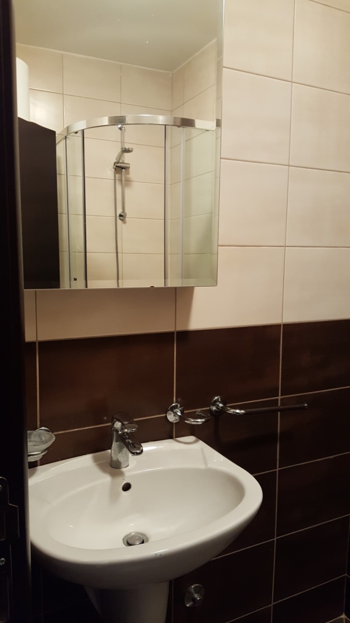 Ванная комната с белой раковиной и душевой кабиной в квартире в Будве, Черногория. Современная отделка плиткой.