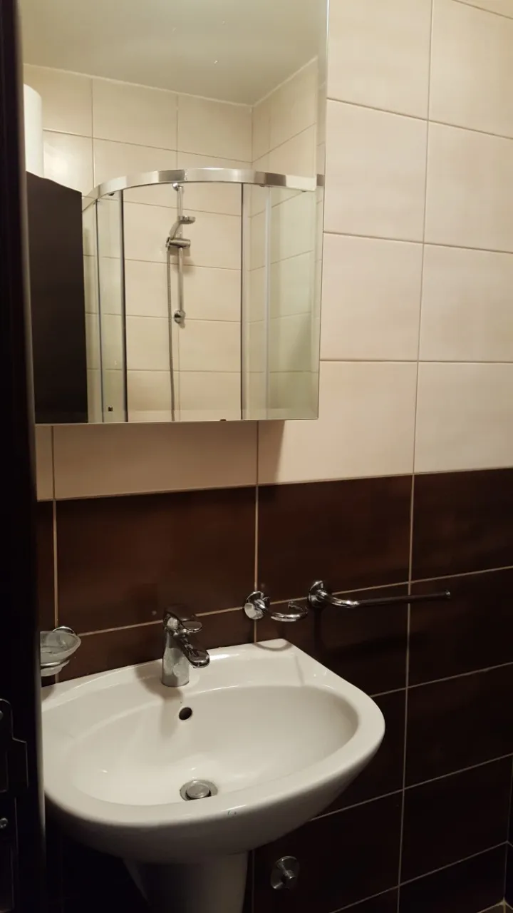 White pedestal sink with chrome faucet, mirror reflecting a glass shower enclosure on two-tone tiled walls.