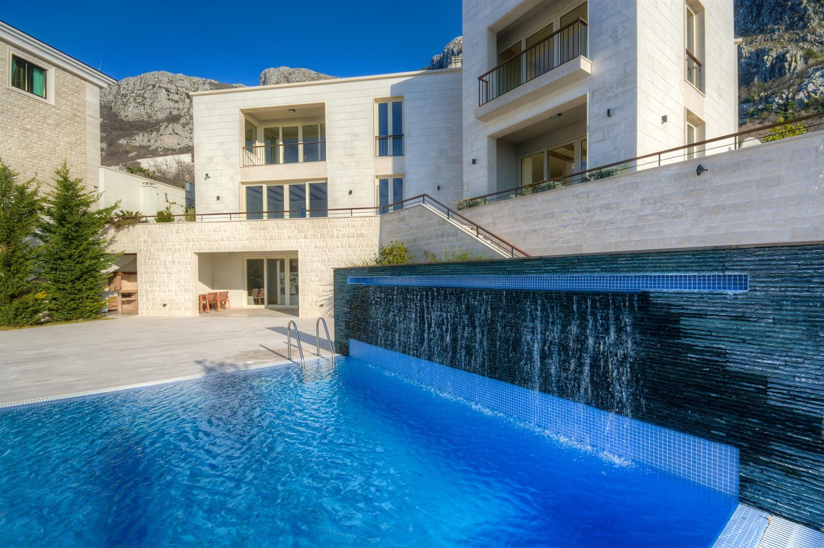 Modern villa with a pool and waterfall in Blizikuće, Montenegro: stone facade and panoramic mountain view.