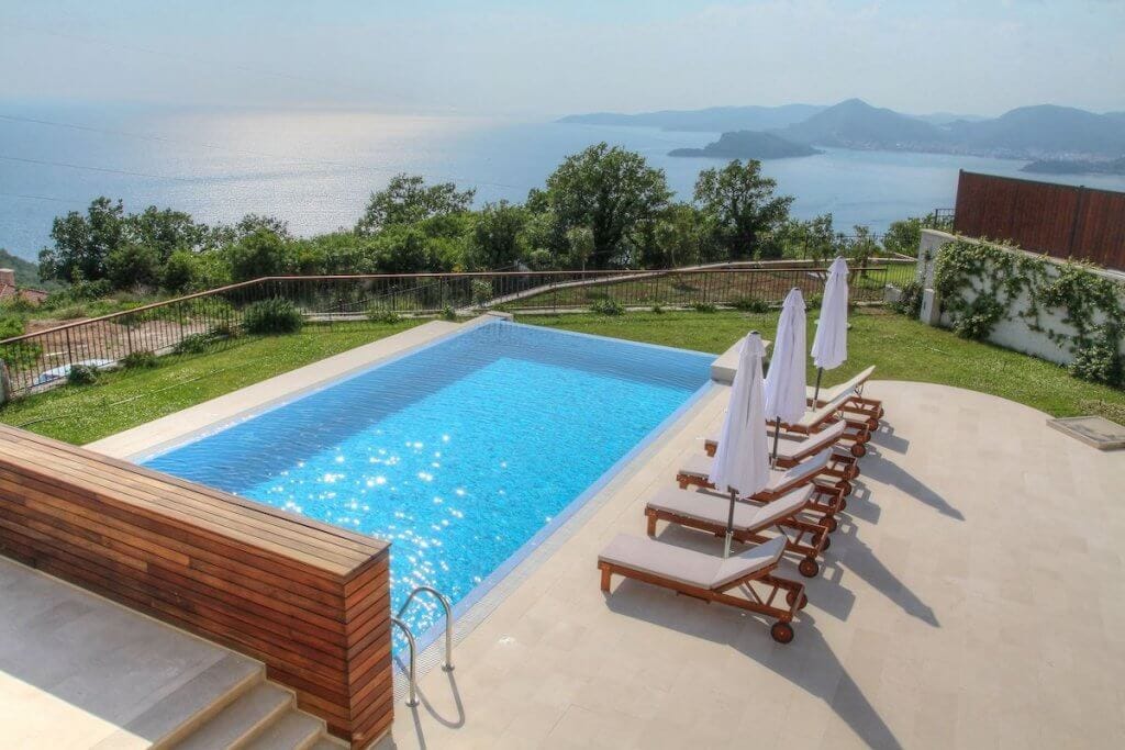 Swimming pool with panoramic sea view at a villa in Blizikuće, Montenegro: sun loungers, umbrellas, and a stone-finished terrace.