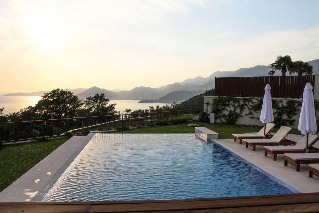 Infinity pool with sea and mountain views at a villa in Blizikuće, Montenegro, with sun loungers and a relaxation area by the water.