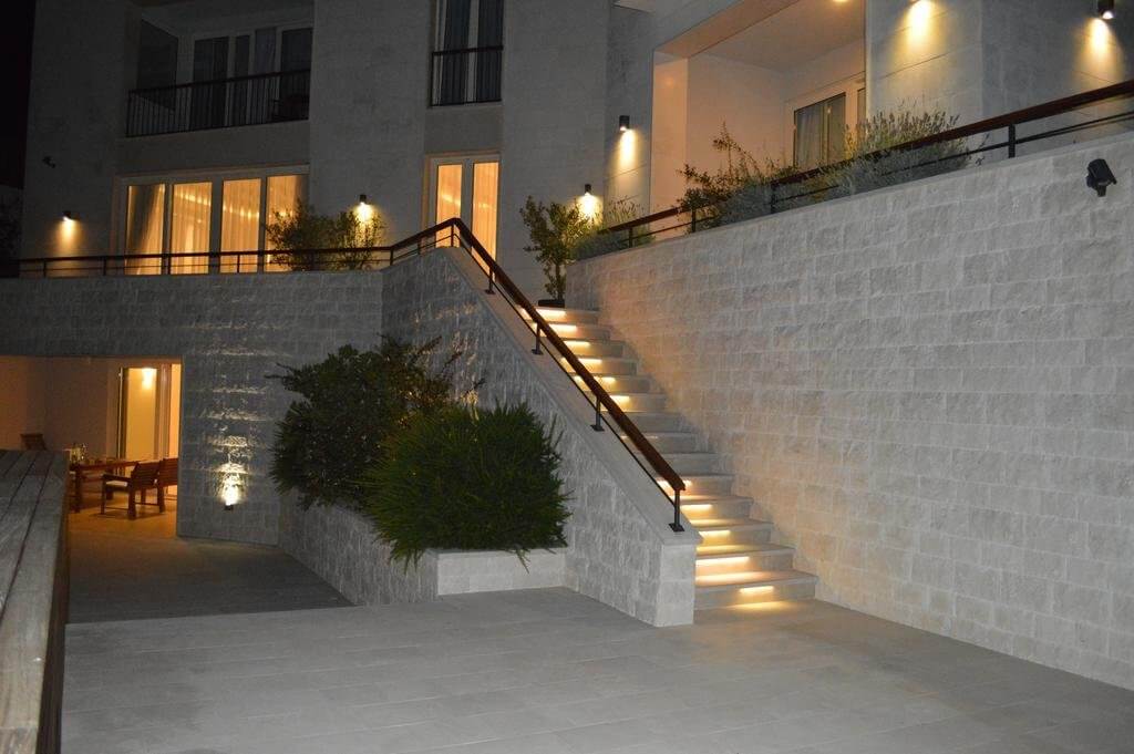 Evening lighting of the villa’s facade and stone staircase in Blizikuće, Montenegro. Modern architecture and landscaping.