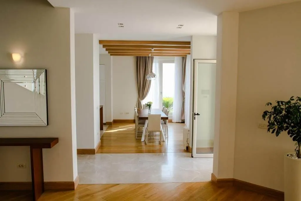 Living room with dining area, wooden floors, wall mirror, and decorative ceiling beams visible.