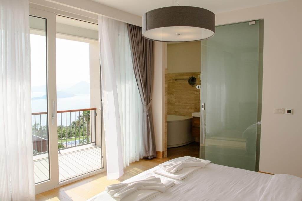 Bedroom in a villa in Blizikuće, Montenegro: panoramic sea view, balcony, glass partition, and bathroom.