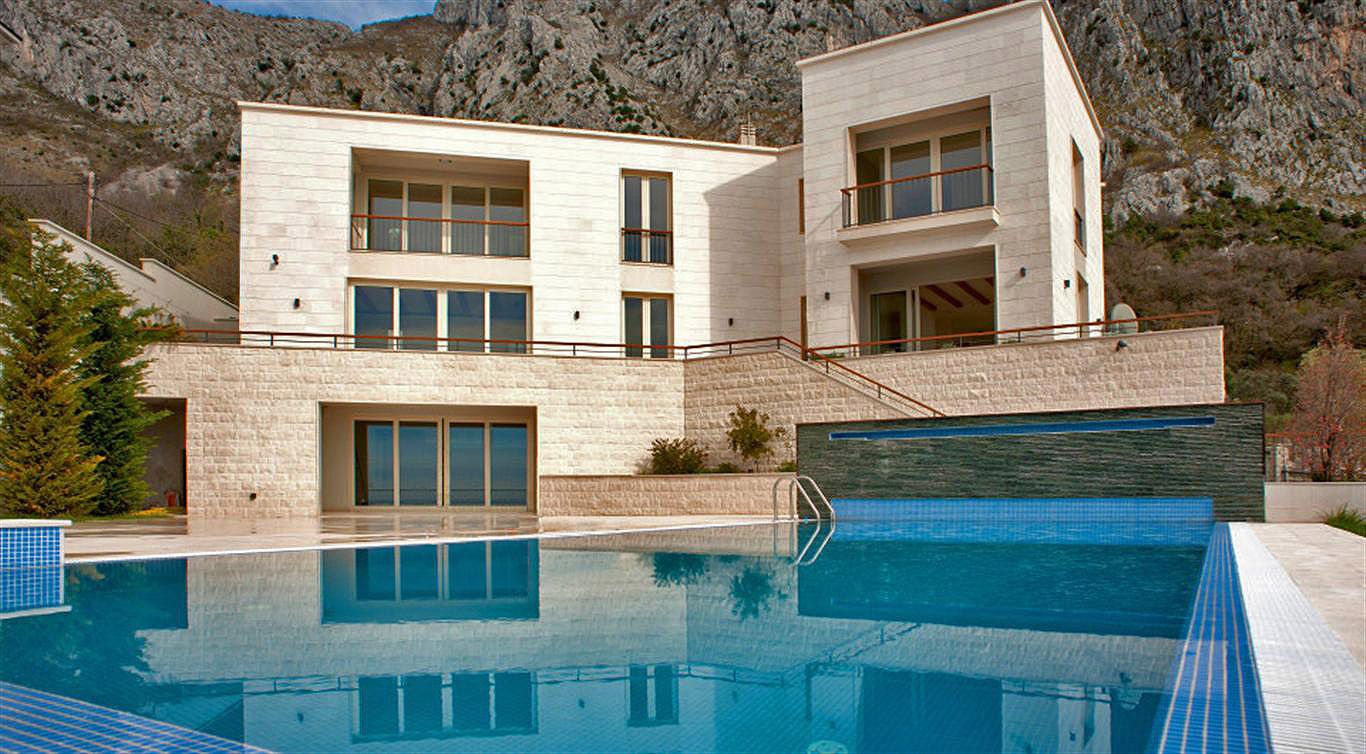 Modern villa with a swimming pool and stone facade finish in Blizikuće, Montenegro, against a backdrop of mountain slopes.