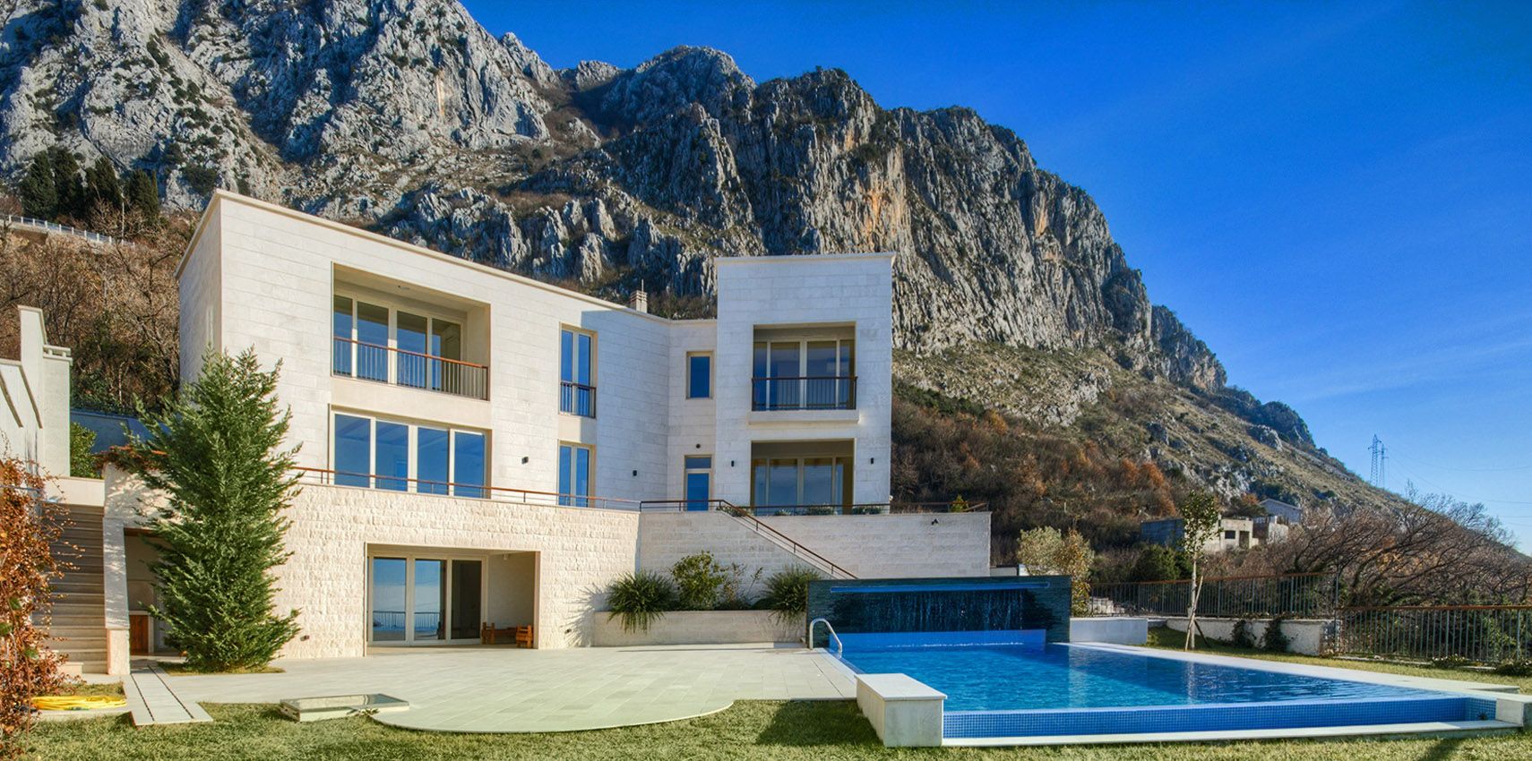 Modern villa with a swimming pool and stone facade finish against a mountain backdrop in Blizikuće, Montenegro.