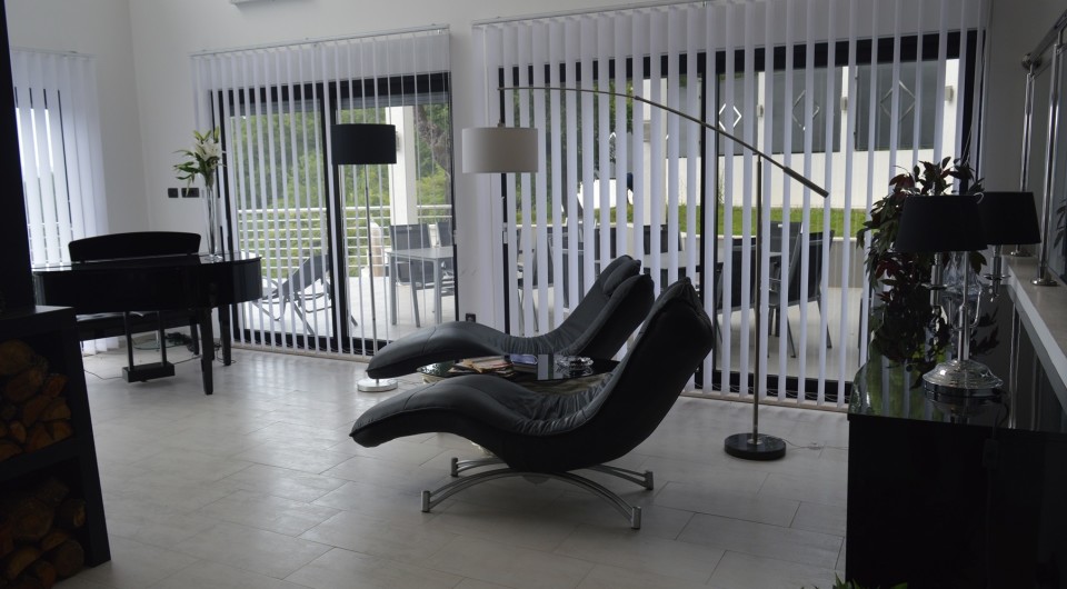 Modern living room in a villa in Tivat, Montenegro: black leather chaise lounges, a grand piano, panoramic windows, and a terrace.