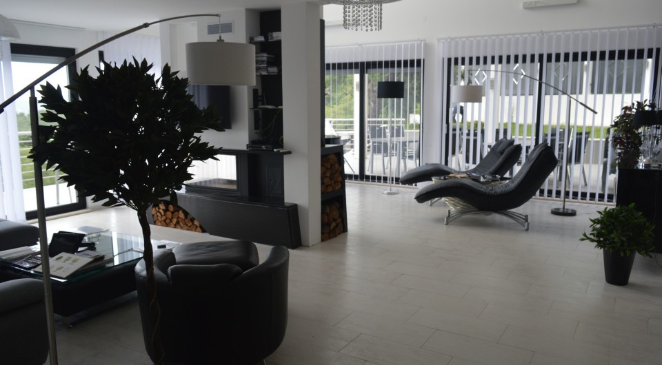 Modern living room in a villa in Tivat, Montenegro: leather furniture, a fireplace with firewood, and panoramic windows with a terrace.