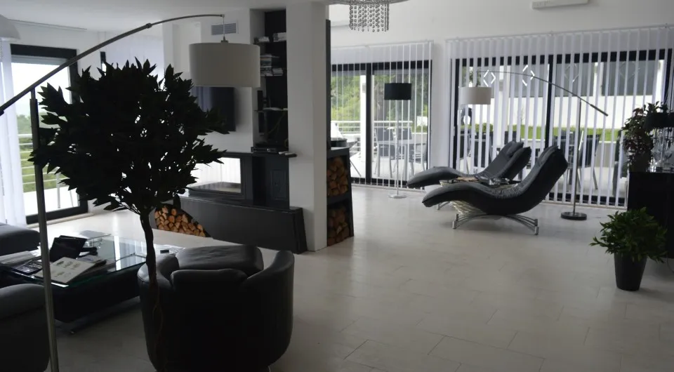 Modern living room featuring black lounge chairs, a fireplace with firewood, and large windows with vertical blinds.