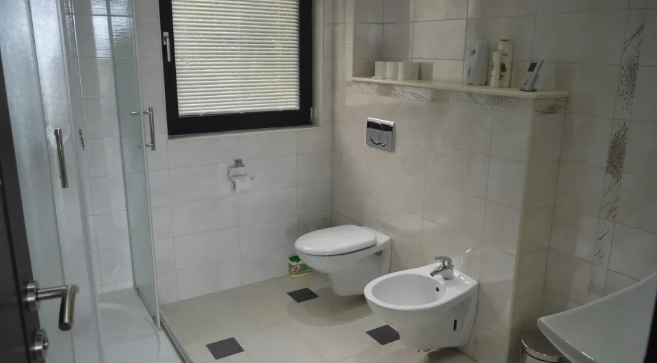 Bathroom featuring a glass shower enclosure, wall-mounted toilet, bidet, and a window with blinds.
