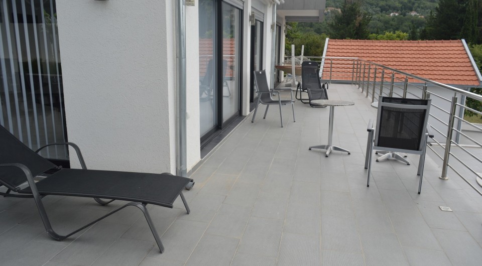 Spacious villa terrace in Tivat, Montenegro, with garden furniture, sun loungers, and panoramic views of green hills.
