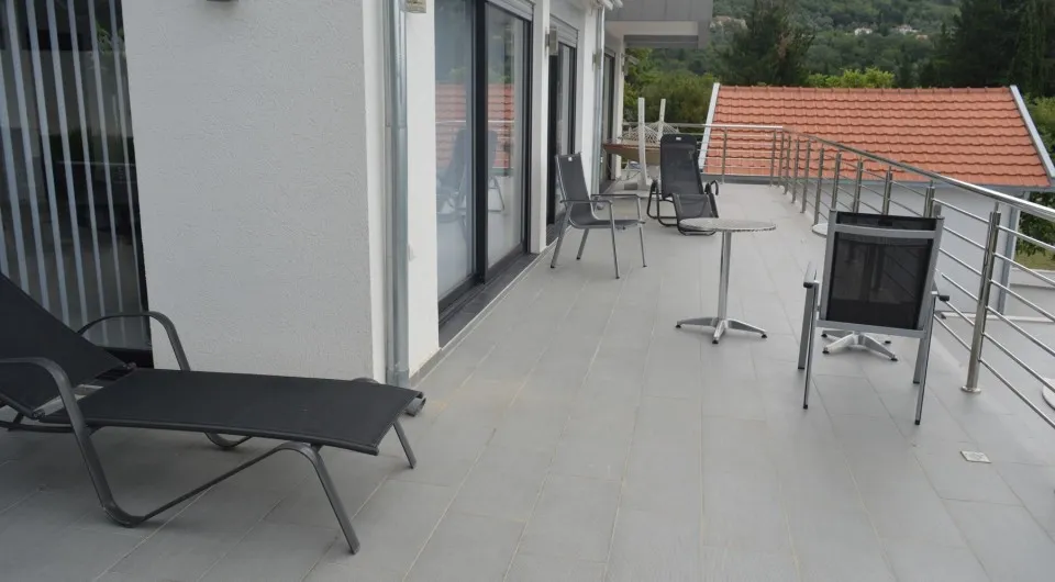 Tiled terrace with metal chairs, a sunbed, and glass doors overlooking a tiled roof.
