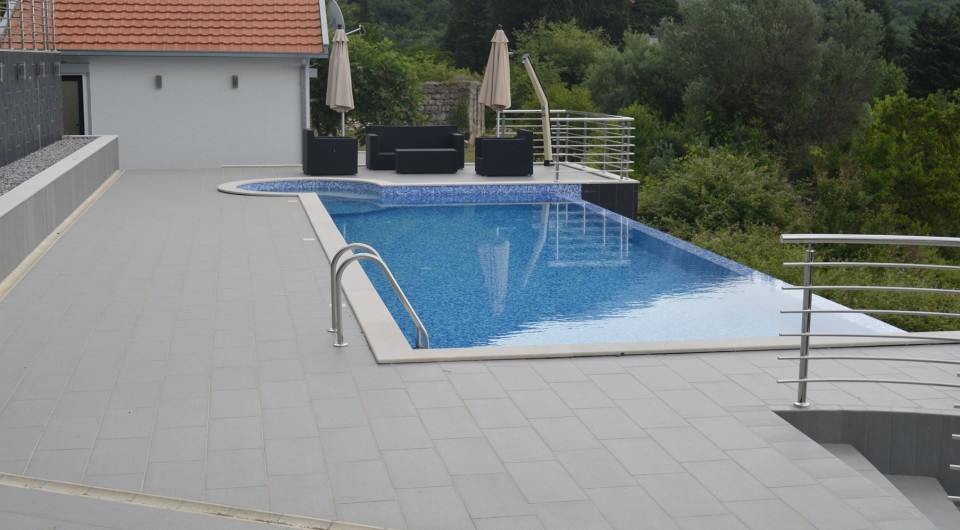 Open-air swimming pool with terrace and lounge area at a villa in Tivat, Montenegro: modern finishes and a view of greenery.