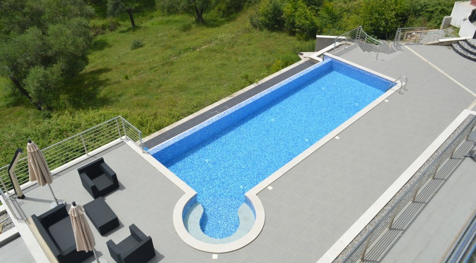Open-air swimming pool with terrace and lounge area at a villa in Tivat, Montenegro: top view of the azure pool and furniture.