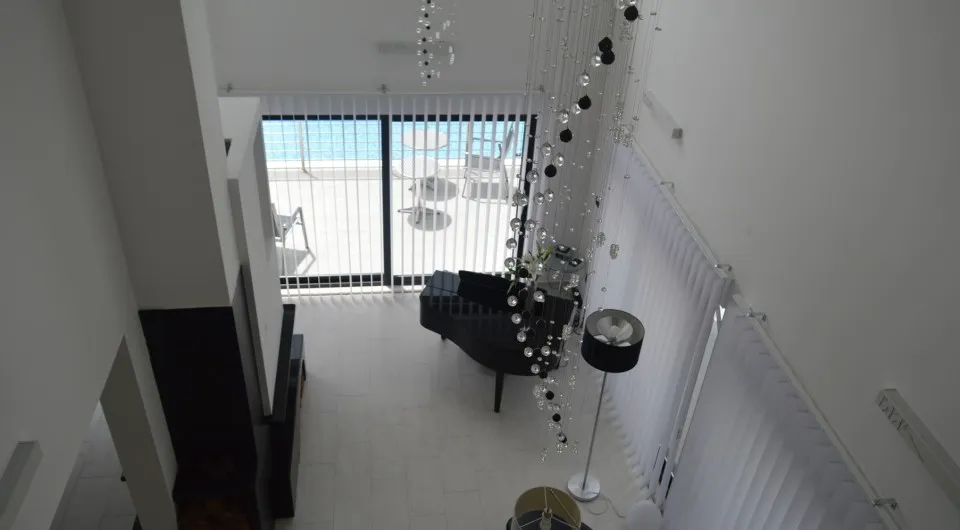 High-angle view of a bright room featuring a black grand piano, chandelier, and pool access.