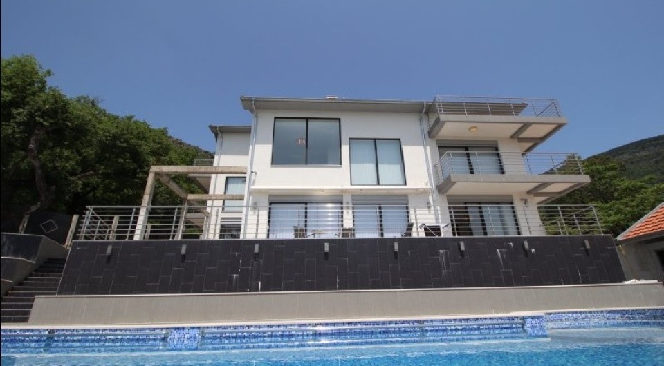 Modern three-story villa with a pool and terraces in Tivat, Montenegro: view of the facade and surrounding grounds.