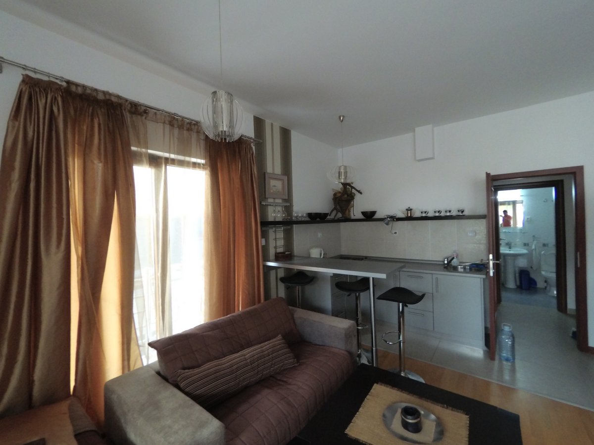 Living room with kitchen and bar counter in an apartment in Budva, Montenegro: modern furniture, light finishes, and access to the balcony.