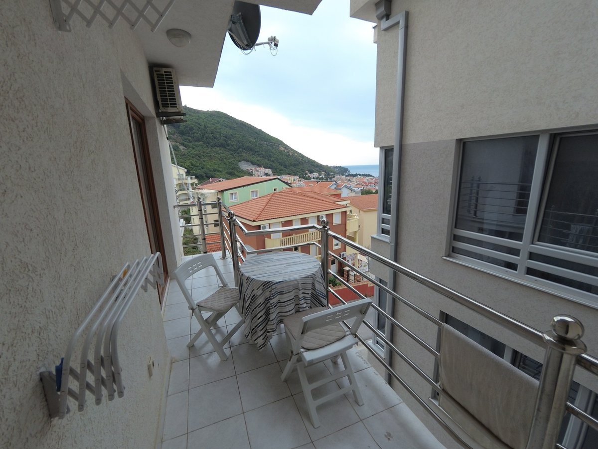 Balcony with furniture and a view of the mountains and sea in an apartment in Budva, Montenegro: table, chairs, and tiled finish.