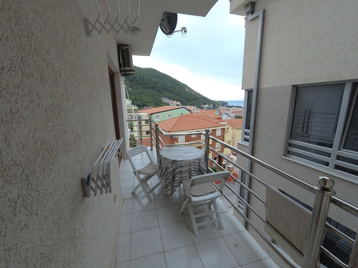 Balcony with furniture and a view of the mountains and the sea in an apartment in Budva, Montenegro. Light finishes and tiled flooring.