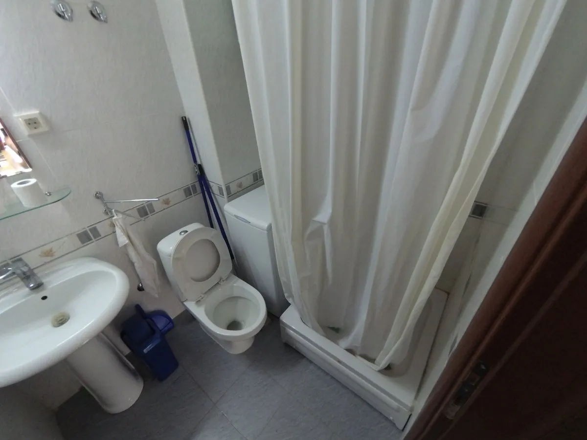 Bathroom featuring a white toilet, pedestal sink, and shower curtain over a tray.