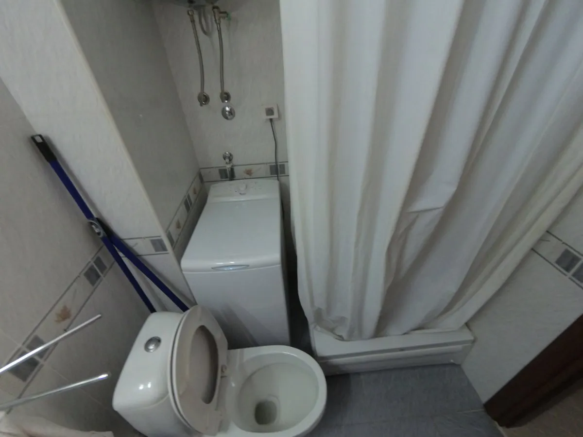 Bathroom with toilet, washing machine, and white shower curtain against tiled walls.