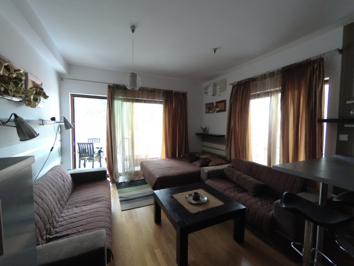 Living room in an apartment in Budva, Montenegro: soft furniture, coffee table, double bed, and access to the terrace.