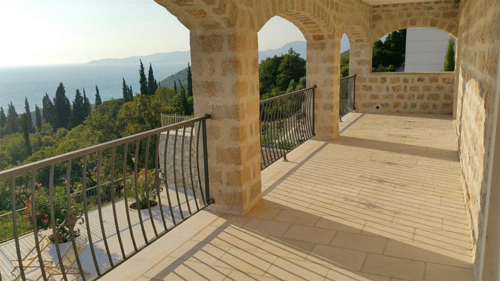 Spacious villa terrace in Drobni Pijesak, Montenegro, with stone arches, wrought-iron railing, and sea view.