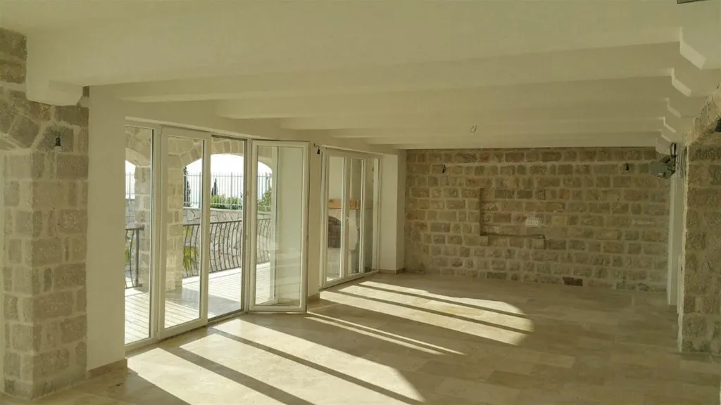 Empty room with stone walls and large glass doors leading to a balcony or terrace.