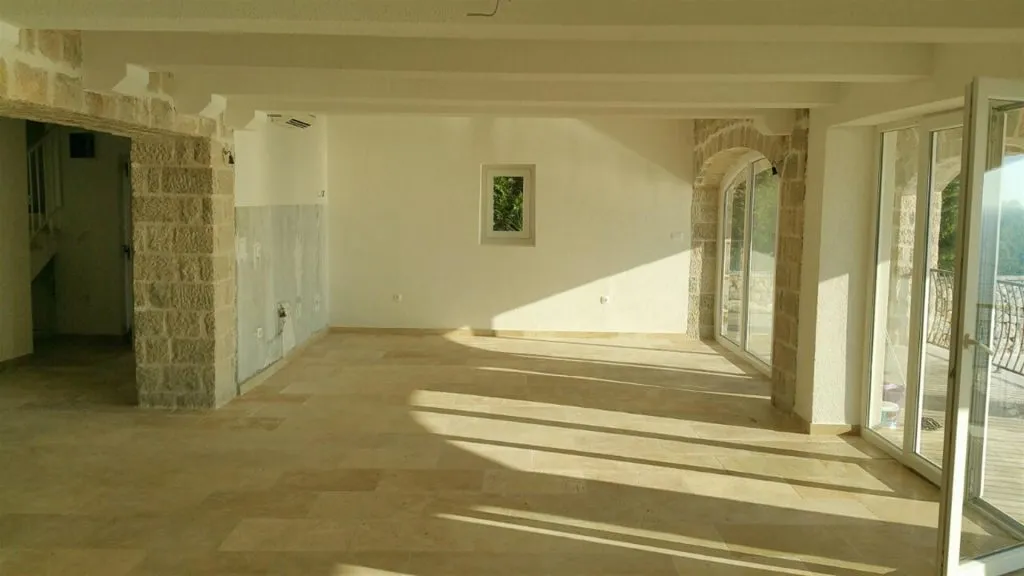Empty room with stone pillars, tiled floor, and large glass doors leading to an outdoor balcony area.