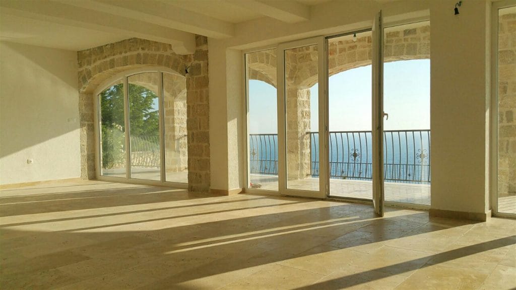 Bright living room in a villa in Drobni Pijesak, Montenegro: stone arches, panoramic windows, and a terrace with sea views.