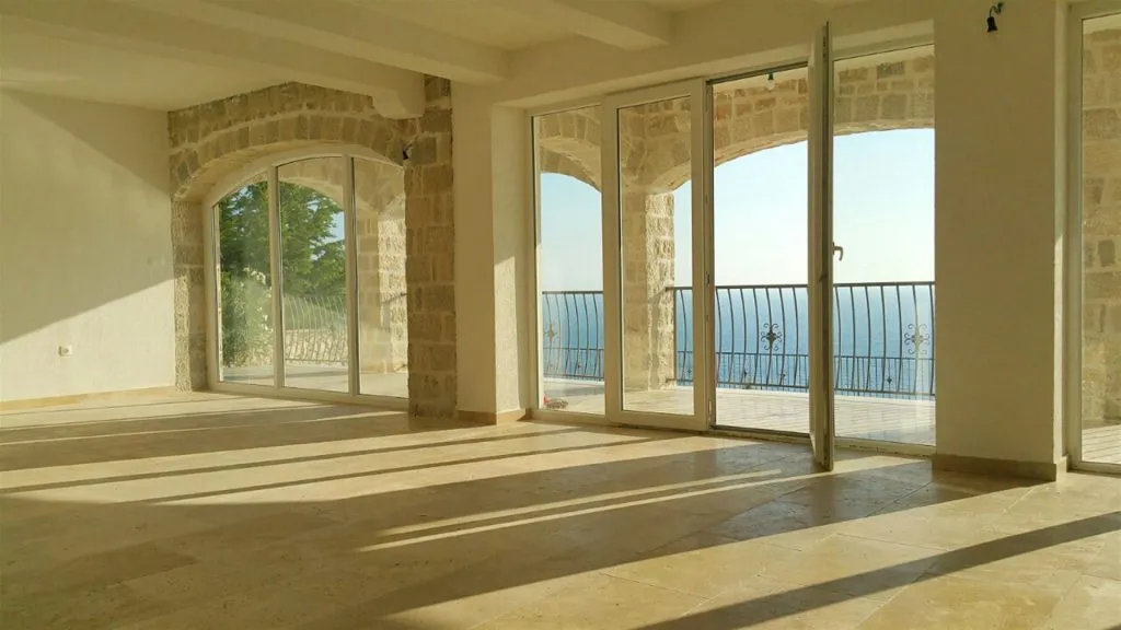 Empty room with stone arches and large glass doors opening to a balcony overlooking the sea.