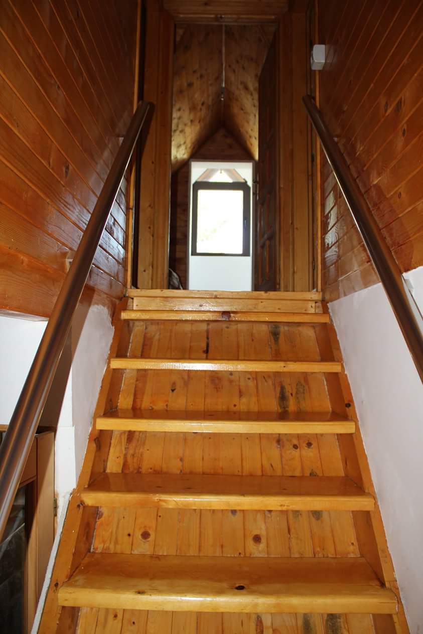 Wooden staircase in a house in Sutomore, Montenegro: natural wood finish and a view of the bright opening to the attic.