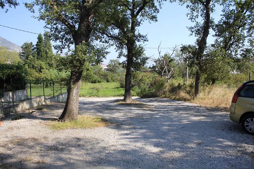 Land plot with a gravel parking area and trees next to a house in Sutomore, Montenegro.