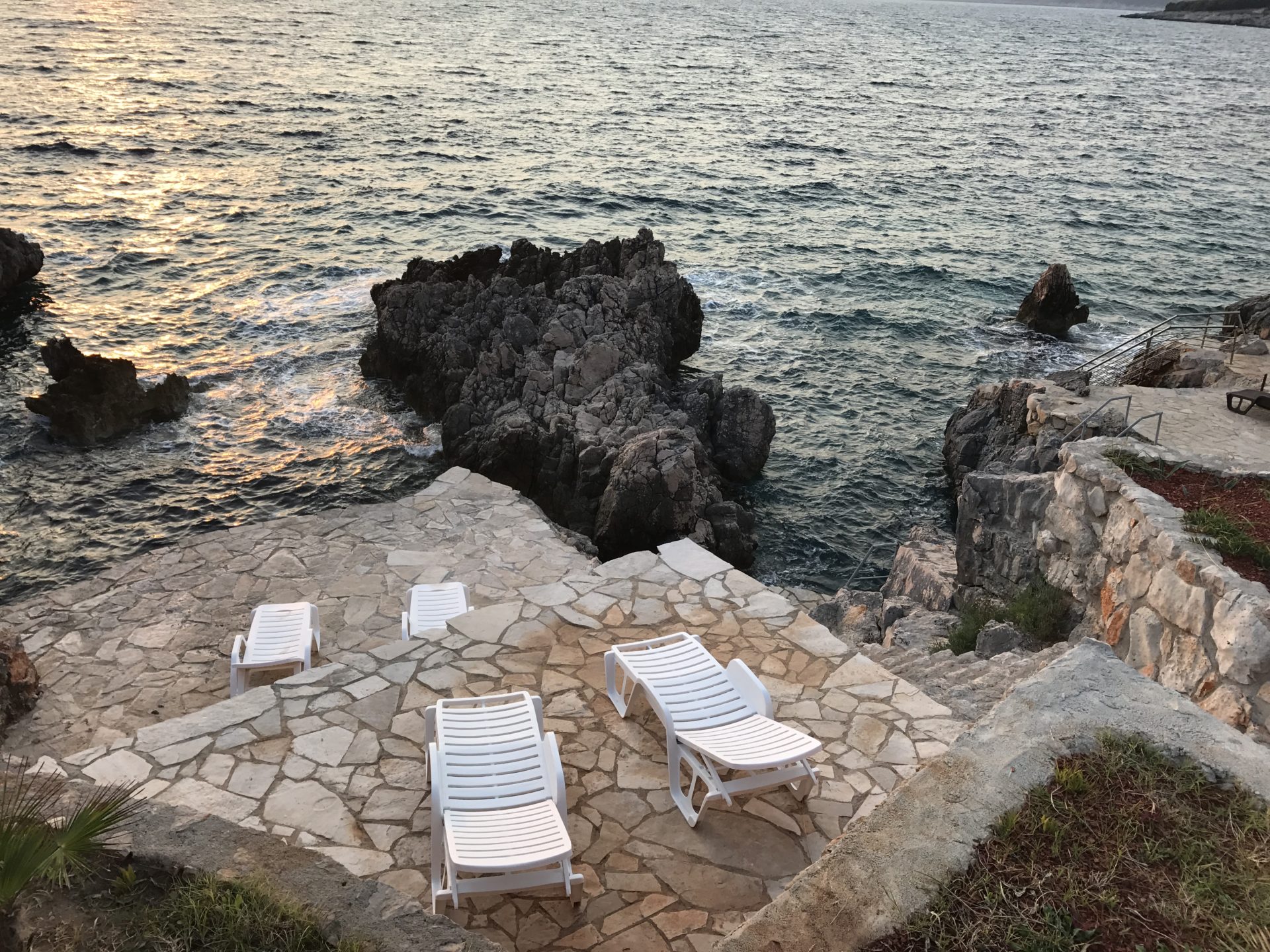 Terrace with sun loungers by the sea at a villa in Utjeha, Montenegro: stone platform, rocky shore, and a view of the Adriatic.