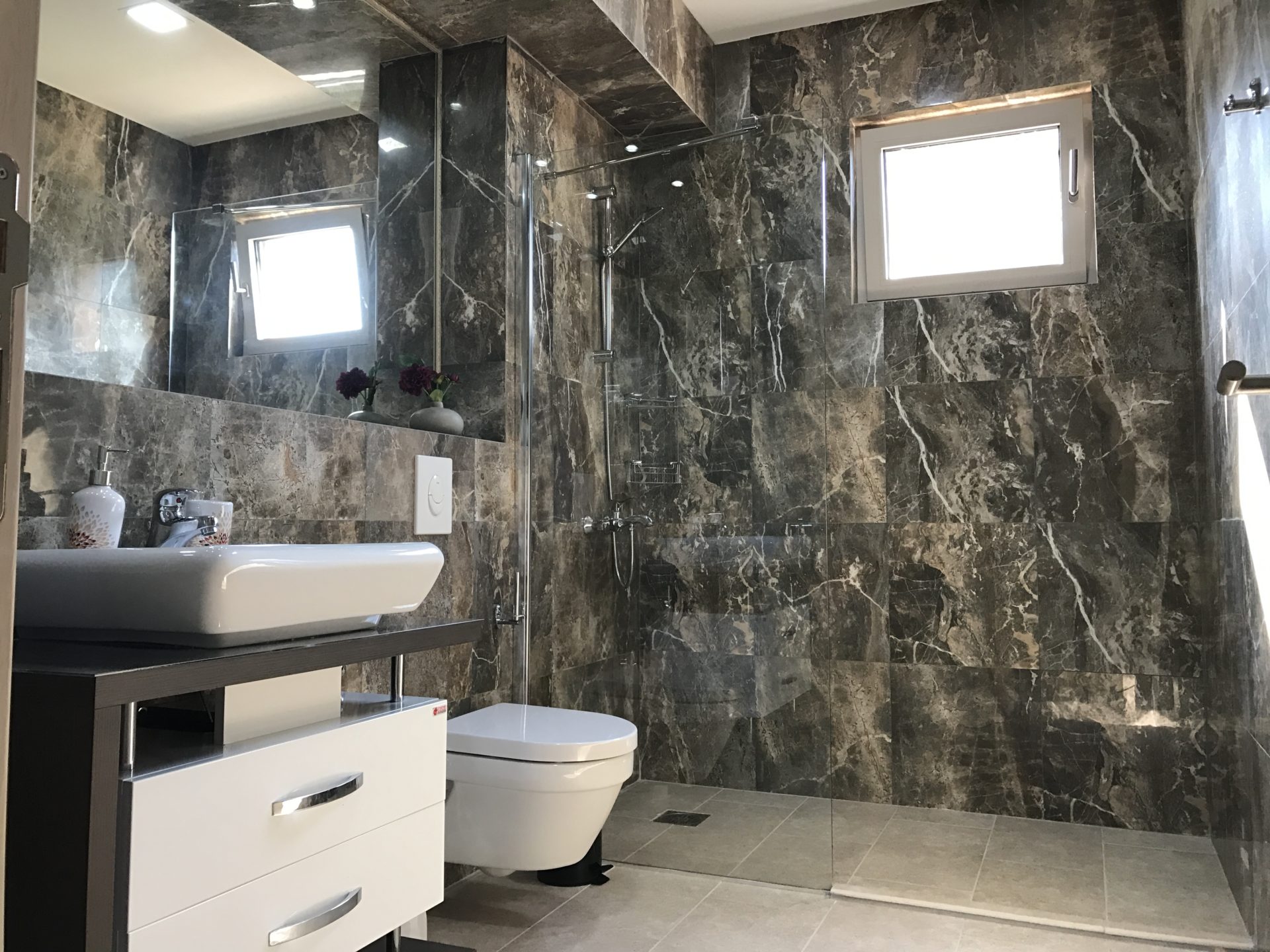Modern bathroom with dark marble finishes and a shower cabin in a villa in Utjeha, Montenegro.