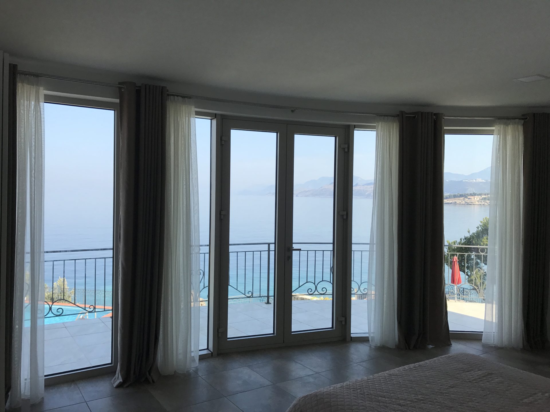 Bedroom with panoramic sea and pool view in a villa in Utjeha, Montenegro: glass doors and terrace.