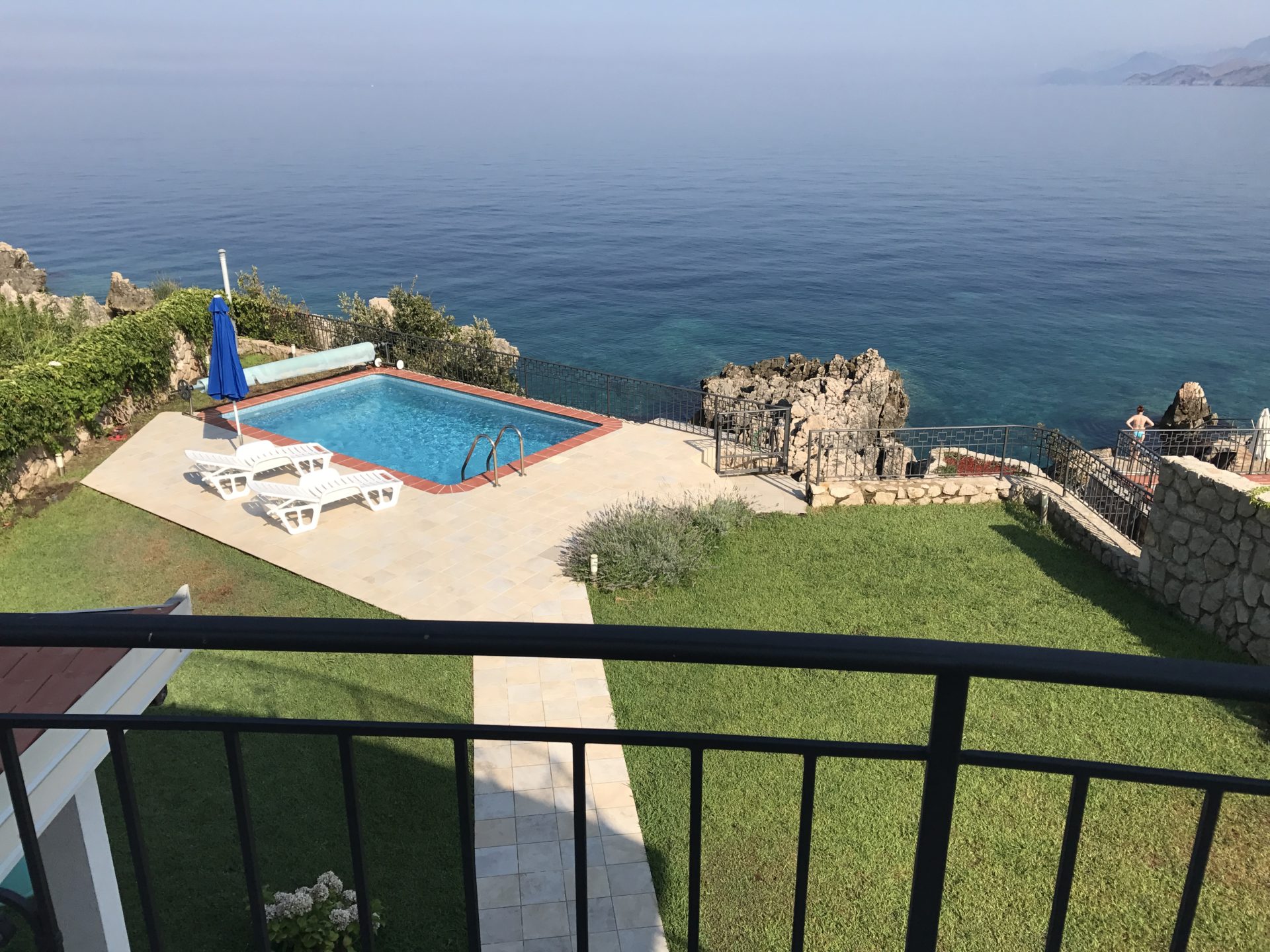 Pool by the sea at a villa in Utjeha, Montenegro: a terrace with sun loungers, a green lawn, and a panoramic view of the Adriatic.