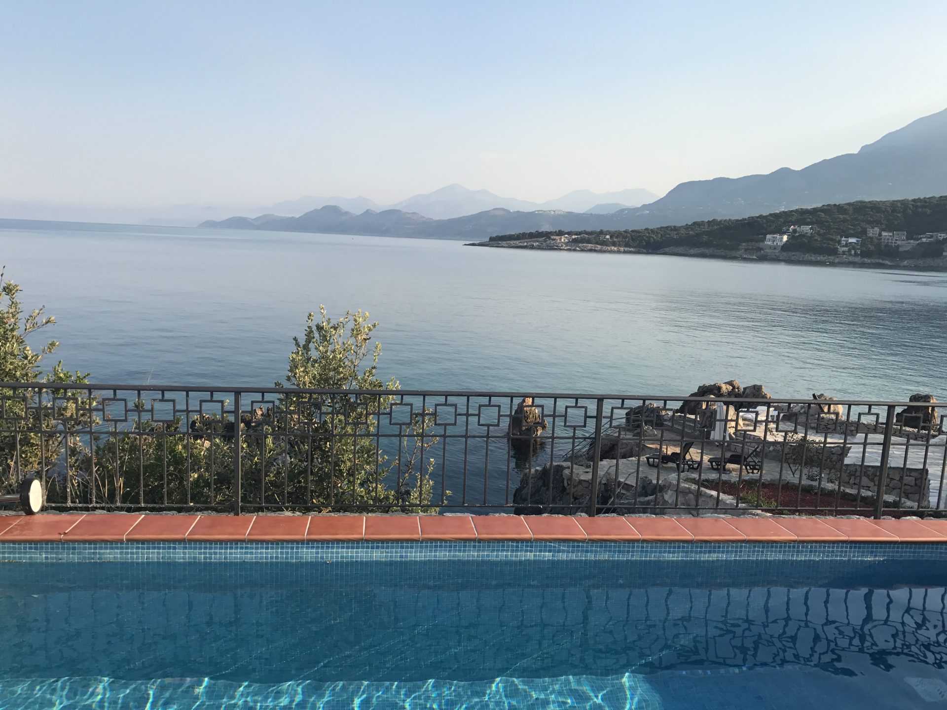 Sea and mountain view from the villa pool in Utjeha, Montenegro: panoramic terrace with railing and a relaxation area by the water.