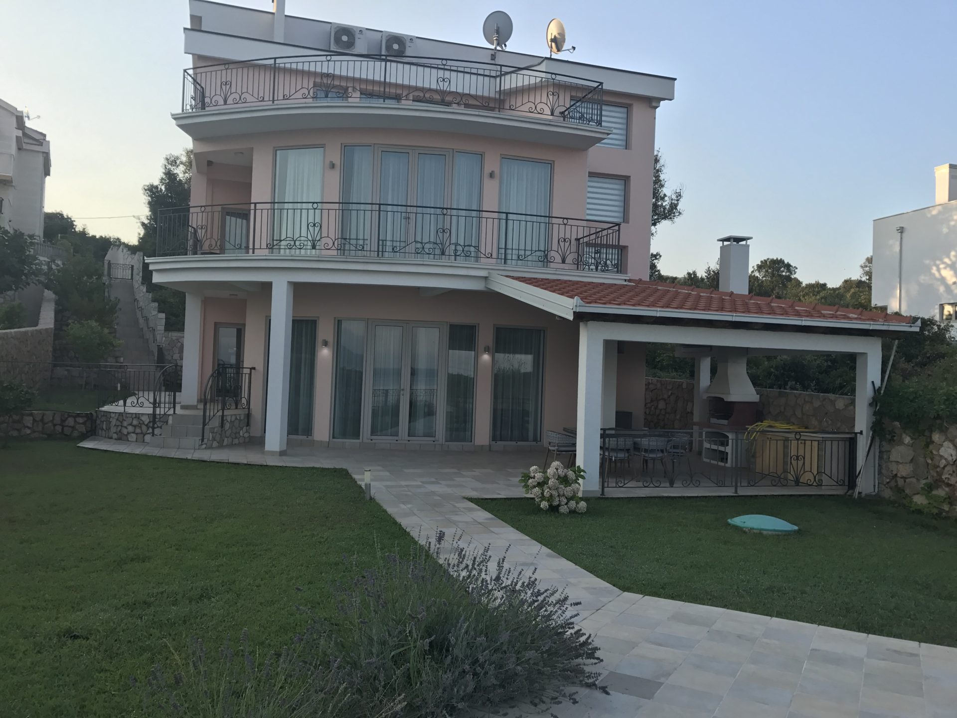 Three-story villa in Utjeha, Montenegro: facade with terraces, panoramic windows, barbecue area, and a well-kept garden.