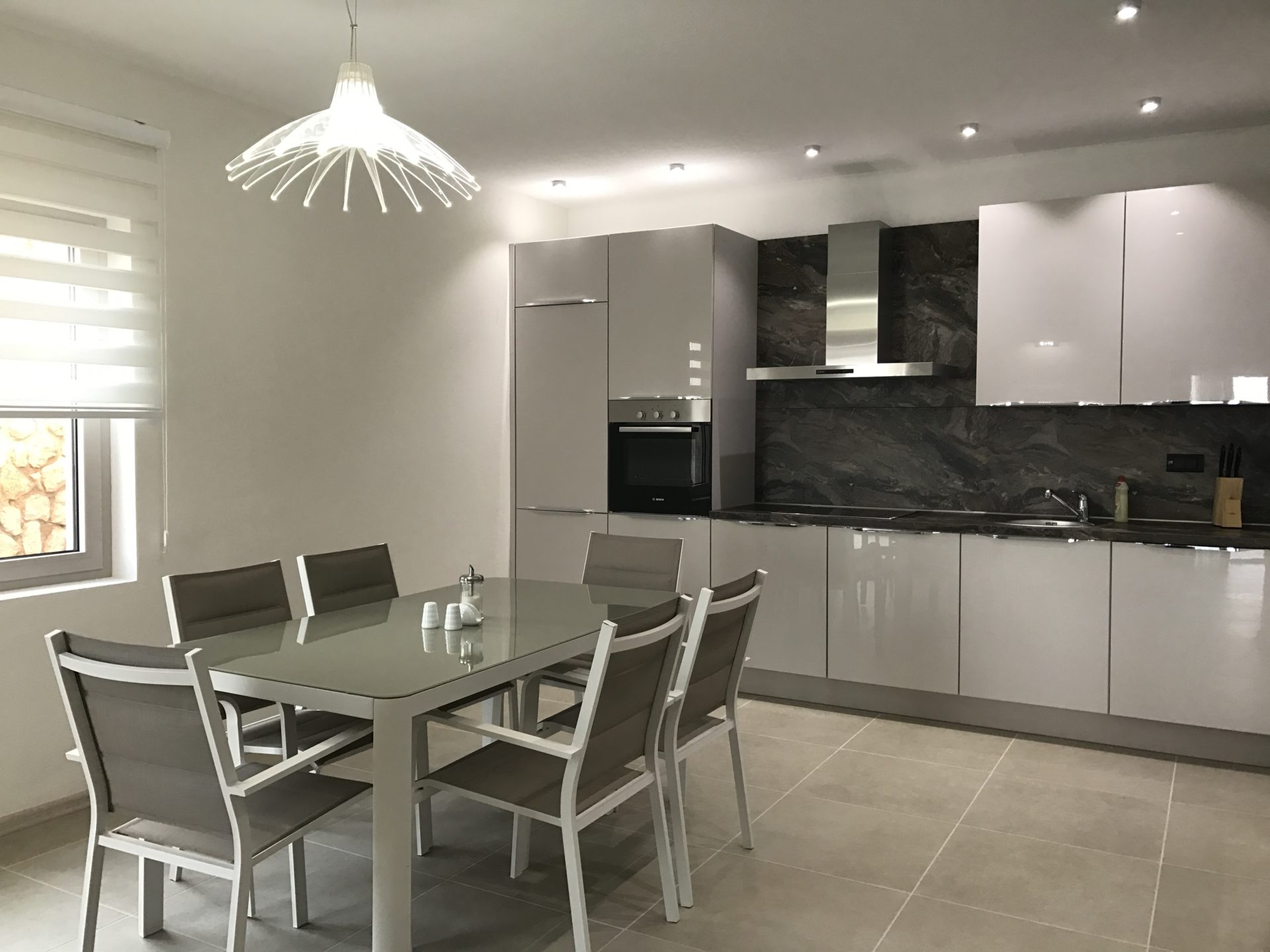 Modern kitchen-dining room in a villa in Utjeha, Montenegro: glossy cabinetry, built-in appliances, and a dining set.